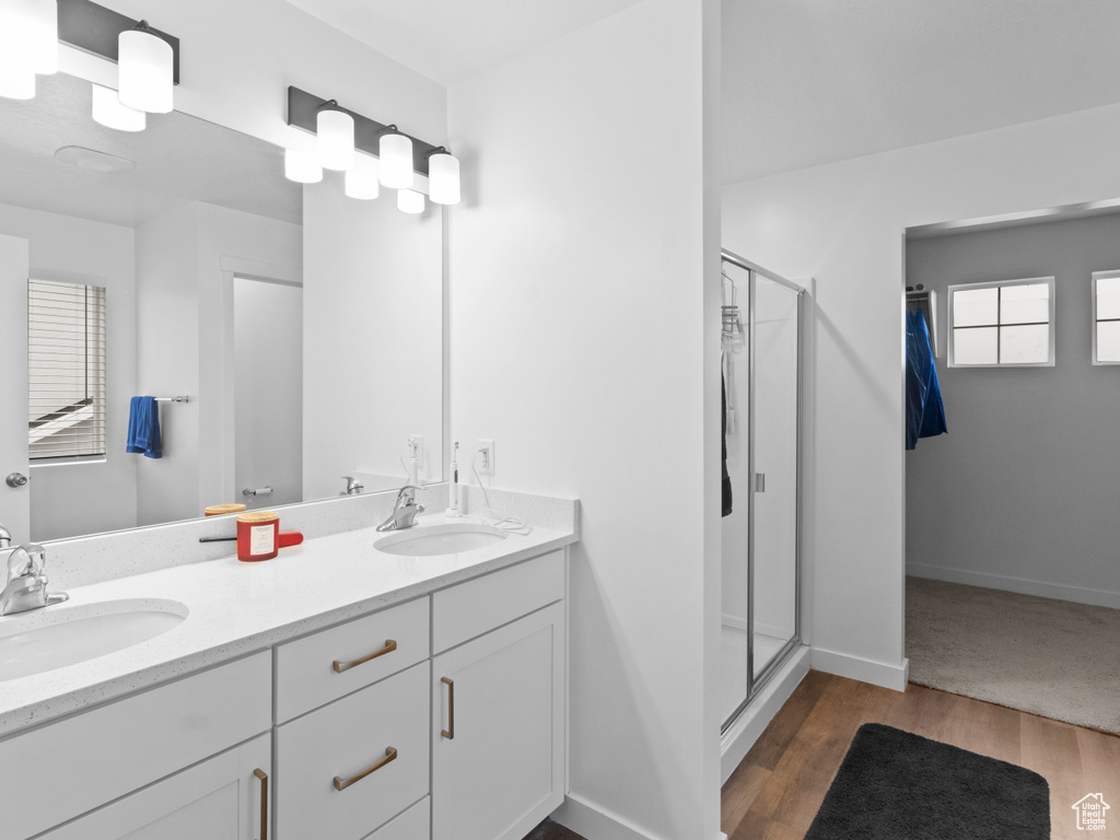 Bathroom featuring a stall shower, wood finished floors, double vanity, and baseboards