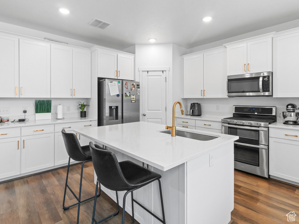 Kitchen with appliances with stainless steel finishes, a sink, white cabinetry, a kitchen breakfast bar, and light countertops