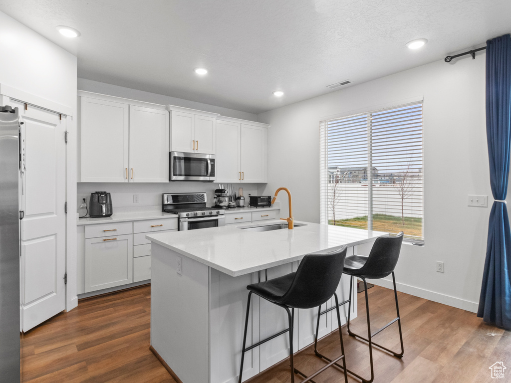 Kitchen with appliances with stainless steel finishes, a sink, white cabinetry, a breakfast bar area, and dark wood-style floors