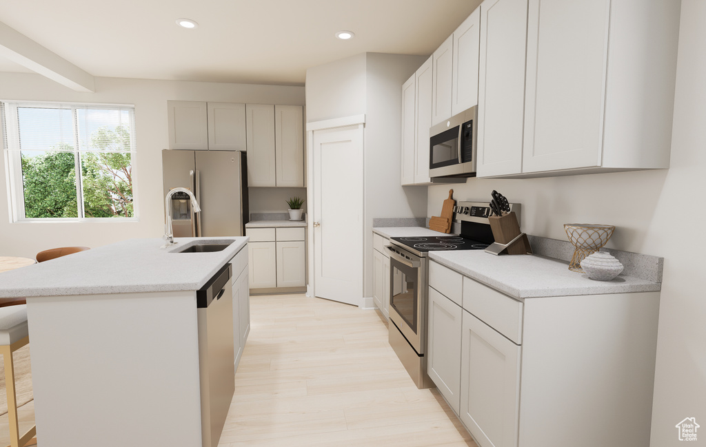 Kitchen with appliances with stainless steel finishes, a sink, a kitchen island with sink, light countertops, and light wood finished floors