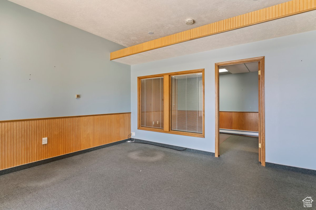 Unfurnished room featuring baseboard heating, wainscoting, wooden walls, carpet flooring, and a smoke detector