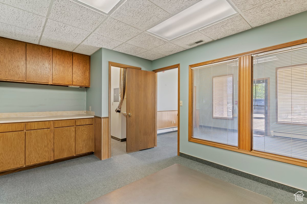 Kitchen featuring a baseboard heating unit, light countertops, brown cabinets, carpet floors, and a drop ceiling