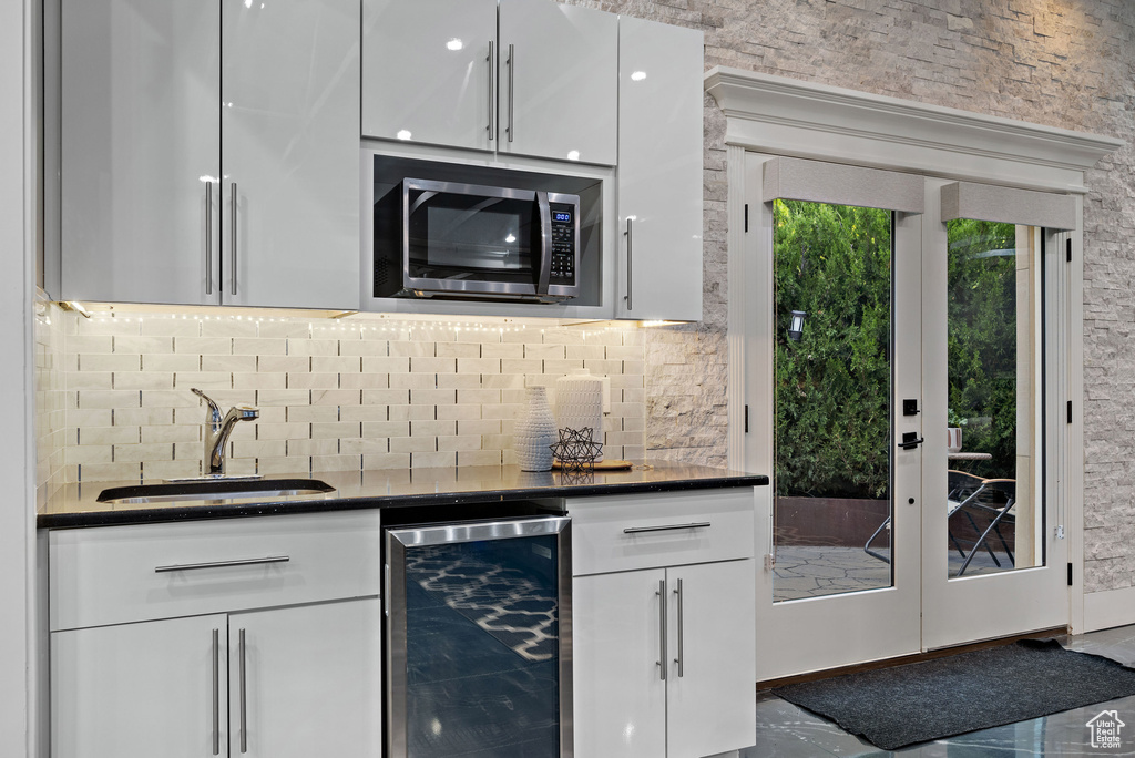 Kitchen with beverage cooler, a sink, stainless steel microwave, white cabinetry, and tasteful backsplash