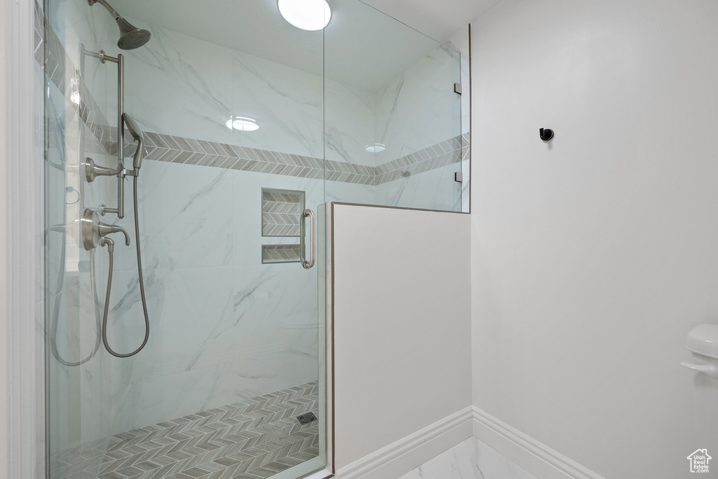 Full bath featuring a marble finish shower, marble finish flooring, and baseboards