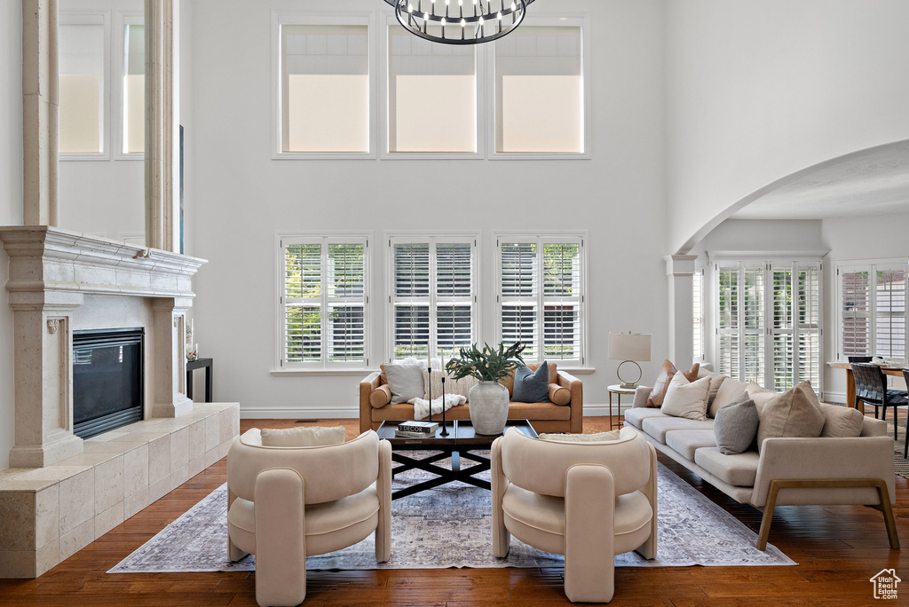 Living room with arched walkways, a high ceiling, a high end fireplace, wood finished floors, and baseboards