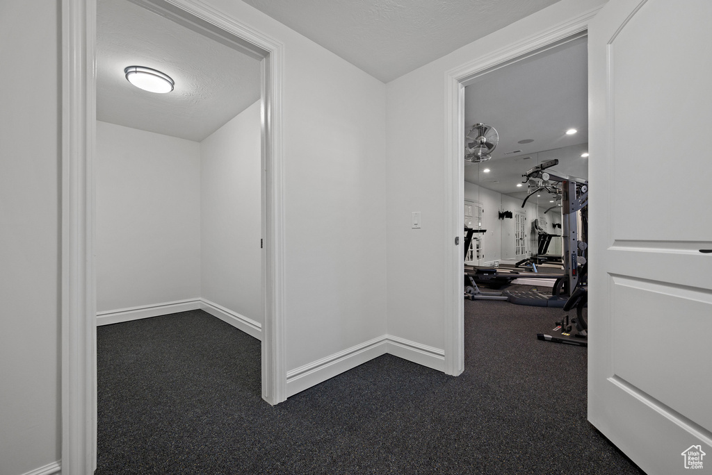 Hall featuring dark colored carpet and baseboards