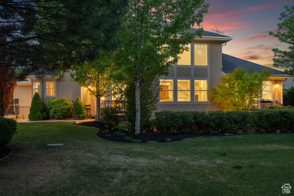 Property exterior at dusk with stucco siding, a yard, and a shingled roof