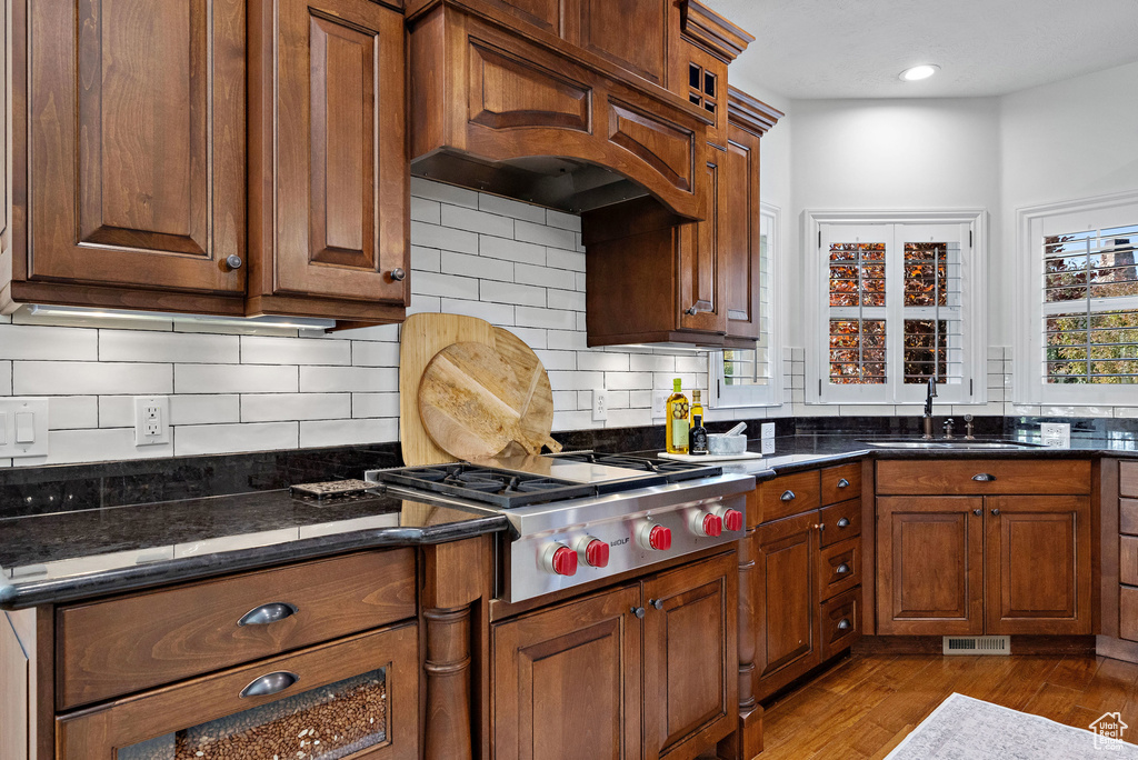 Kitchen with a sink, stainless steel gas cooktop, wood finished floors, custom range hood, and backsplash