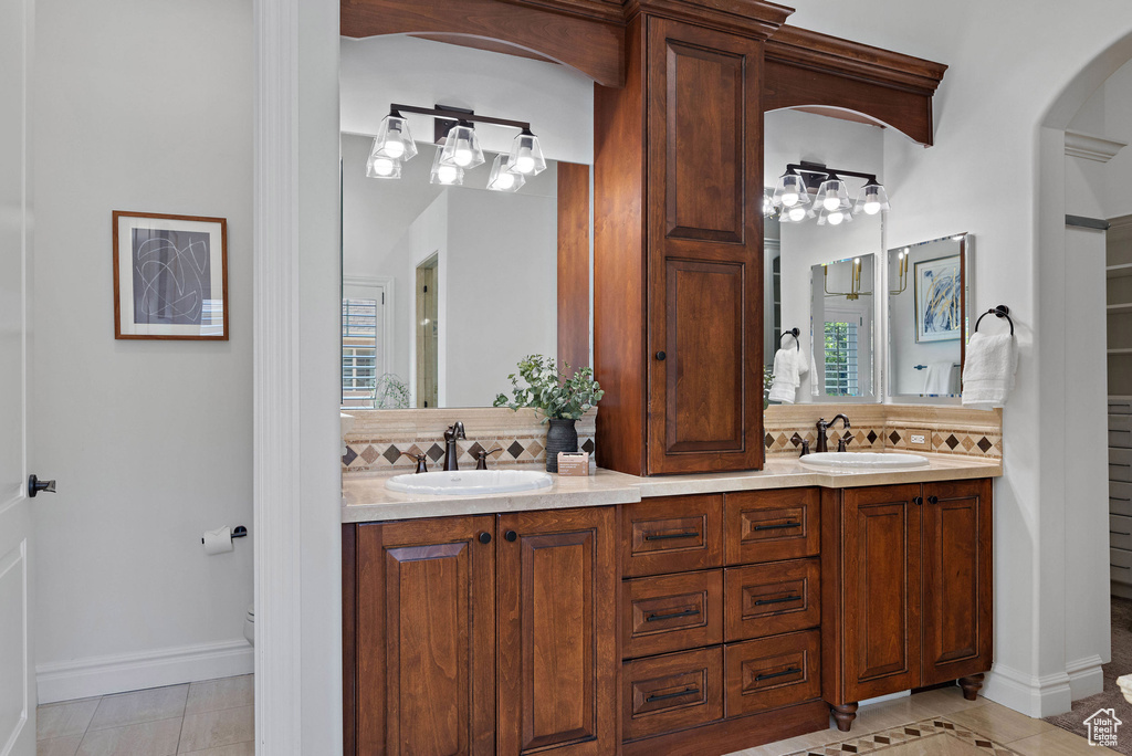 Bathroom with backsplash, tile patterned flooring, toilet, double vanity, and baseboards