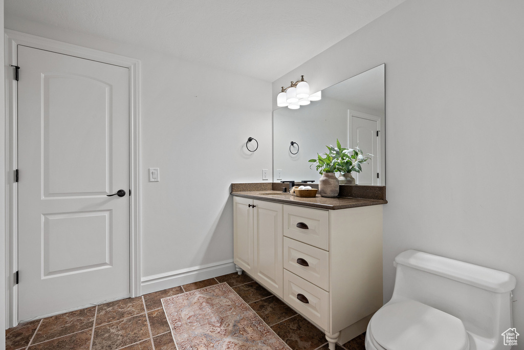 Bathroom with toilet, stone finish floors, vanity, baseboards, and a chandelier