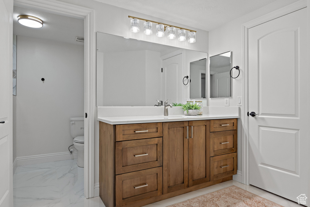 Bathroom with marble finish flooring, vanity, toilet, and baseboards