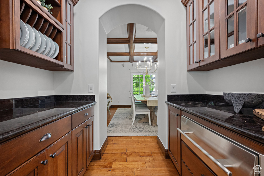 Kitchen with a warming drawer, coffered ceiling, light wood-style floors, dark stone countertops, and a chandelier