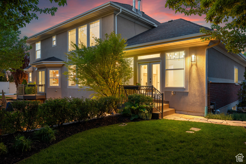 View of front of home featuring stucco siding, french doors, a front lawn, and roof with shingles