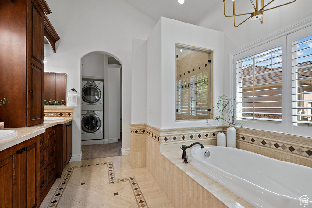 Bathroom featuring estacked washer and dryer, a bath, double vanity, tile patterned flooring, and a chandelier