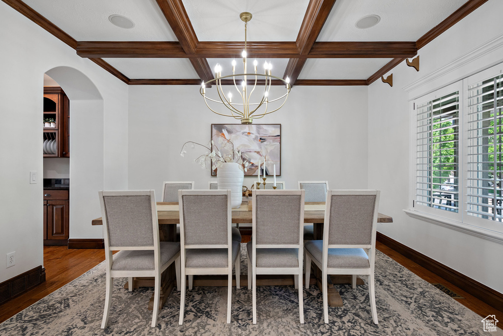Dining area featuring coffered ceiling, arched walkways, a chandelier, dark wood-style floors, and beam ceiling