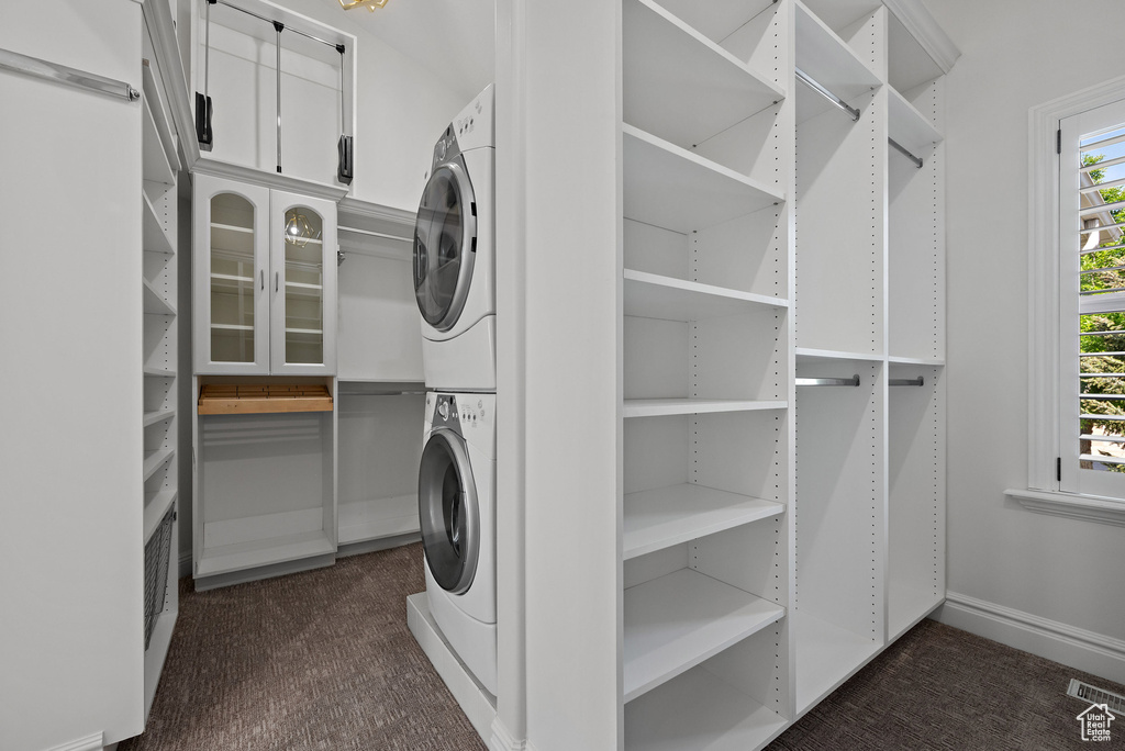 Clothes washing area featuring stacked washing machine and dryer, dark carpet, and baseboards