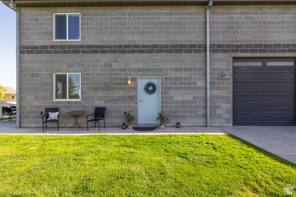 View of exterior entry featuring concrete block siding, a lawn, and a patio