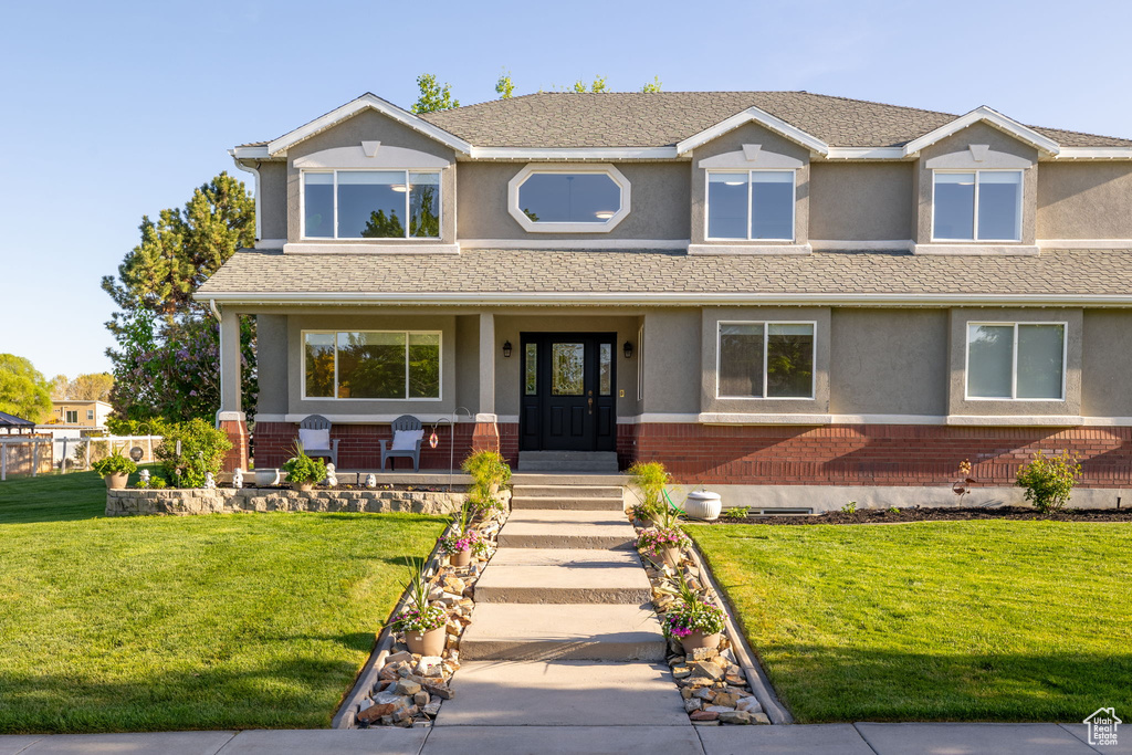 View of front facade featuring brick siding, stucco siding, covered porch, and a front yard