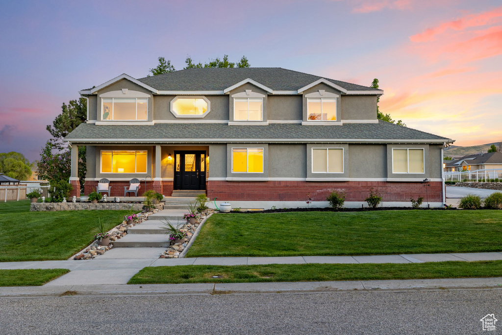 View of front of home featuring brick siding, stucco siding, a yard, and a porch