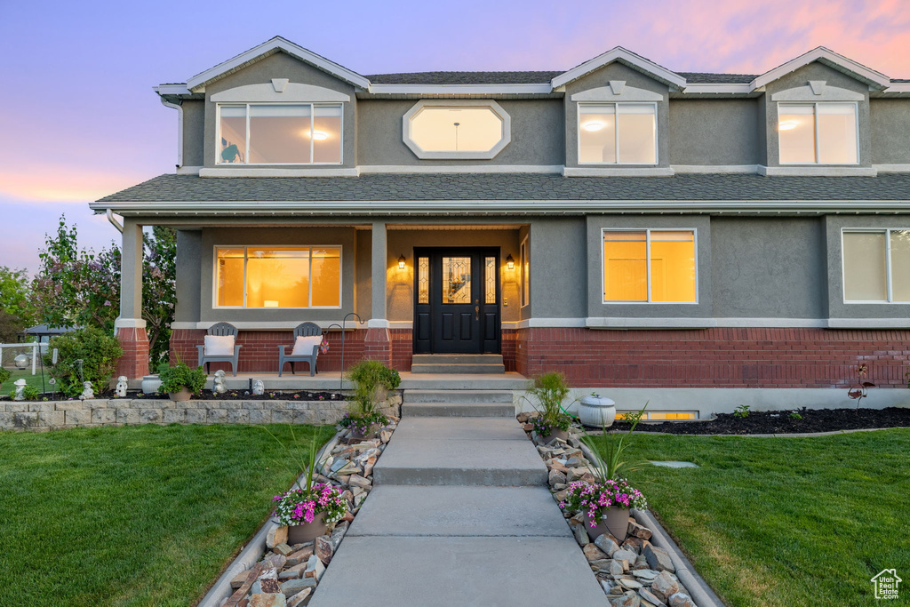 View of front of home with a porch, stucco siding, a front lawn, and brick siding