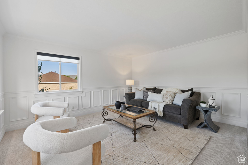 Living area featuring light colored carpet, a wainscoted wall, ornamental molding, and a decorative wall