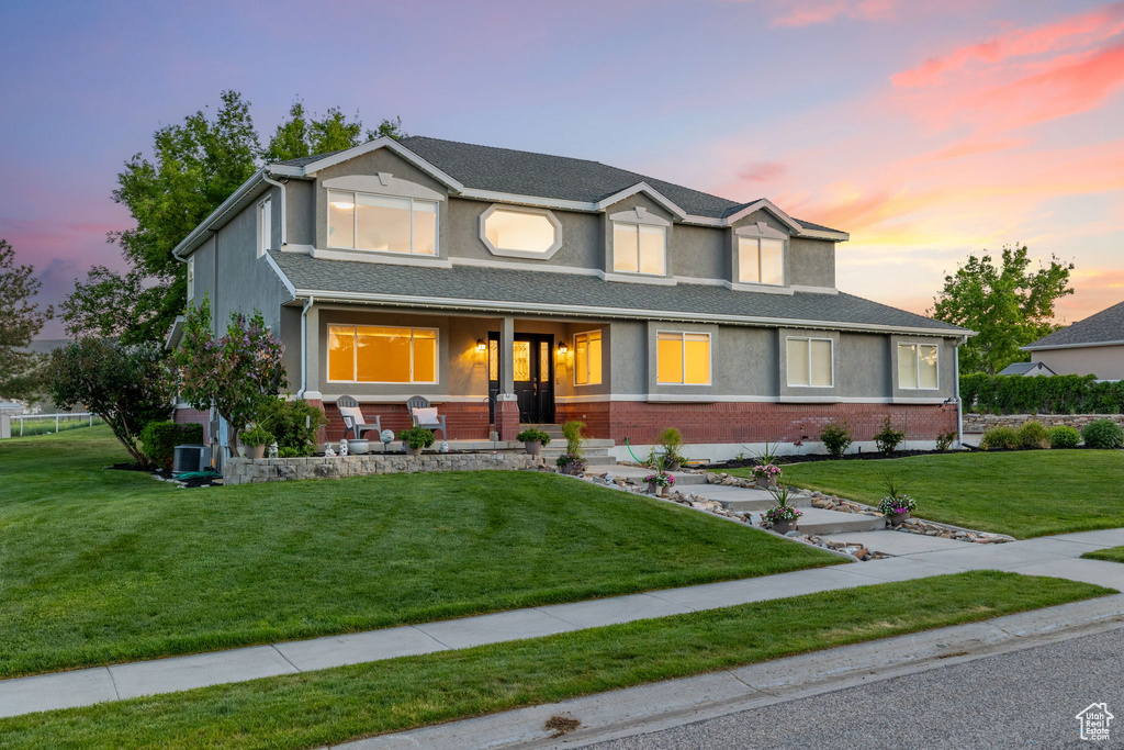 View of front of home with a porch, a yard, stucco siding, and brick siding