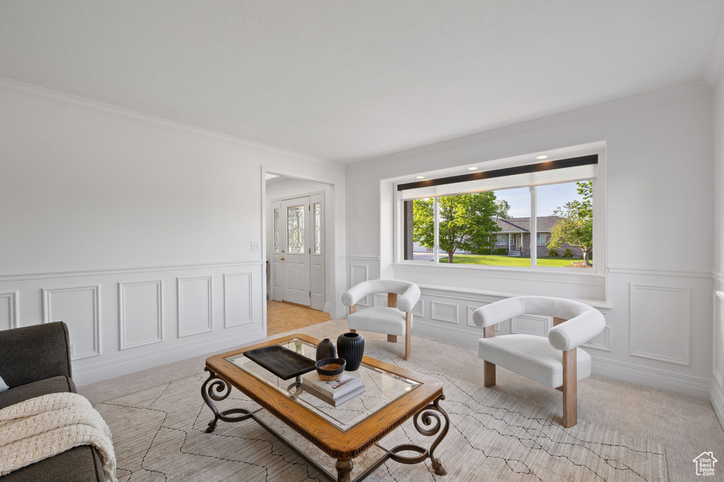 Living room featuring crown molding, light carpet, a decorative wall, and a wainscoted wall
