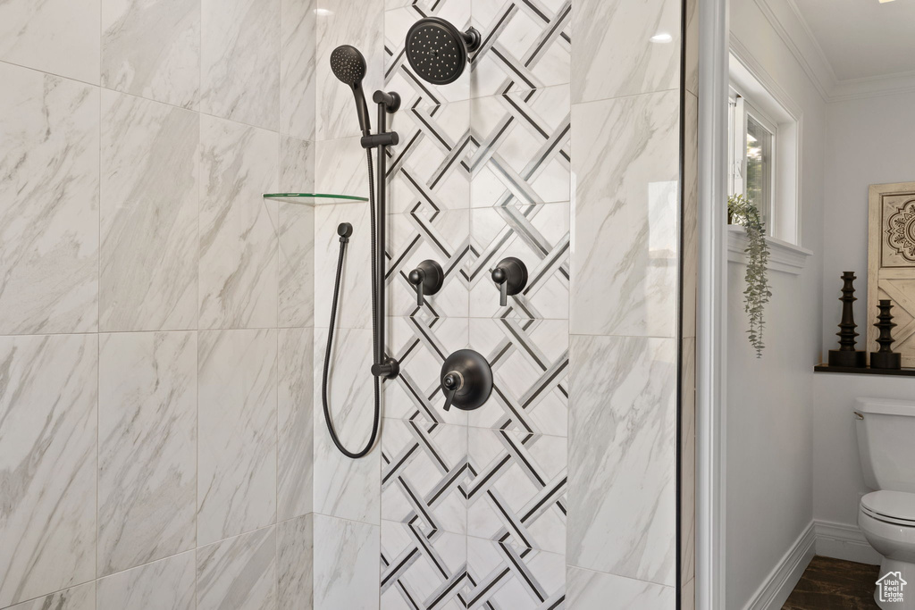 Bathroom with ornamental molding, a tile shower, toilet, and baseboards
