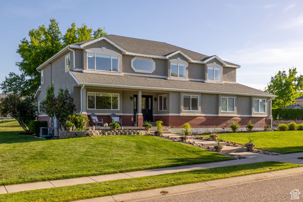 View of front of home featuring a porch, stucco siding, a front lawn, brick siding, and central AC