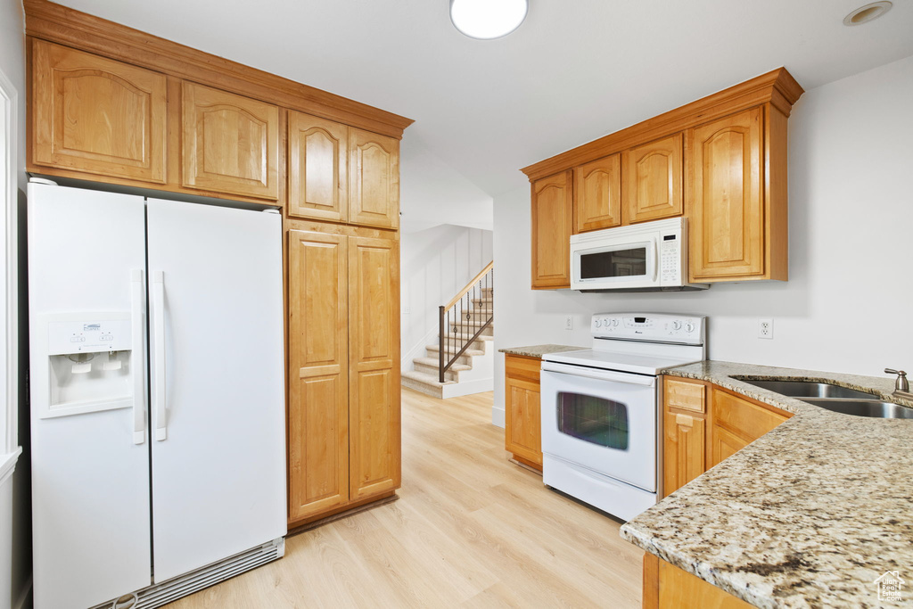 Kitchen with white appliances, light wood-style flooring, light stone countertops, and a sink