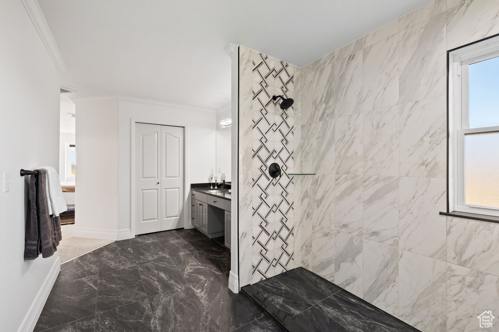 Bathroom with ornamental molding, marble tiled flooring, tiled shower, vanity, and healthy amount of natural light