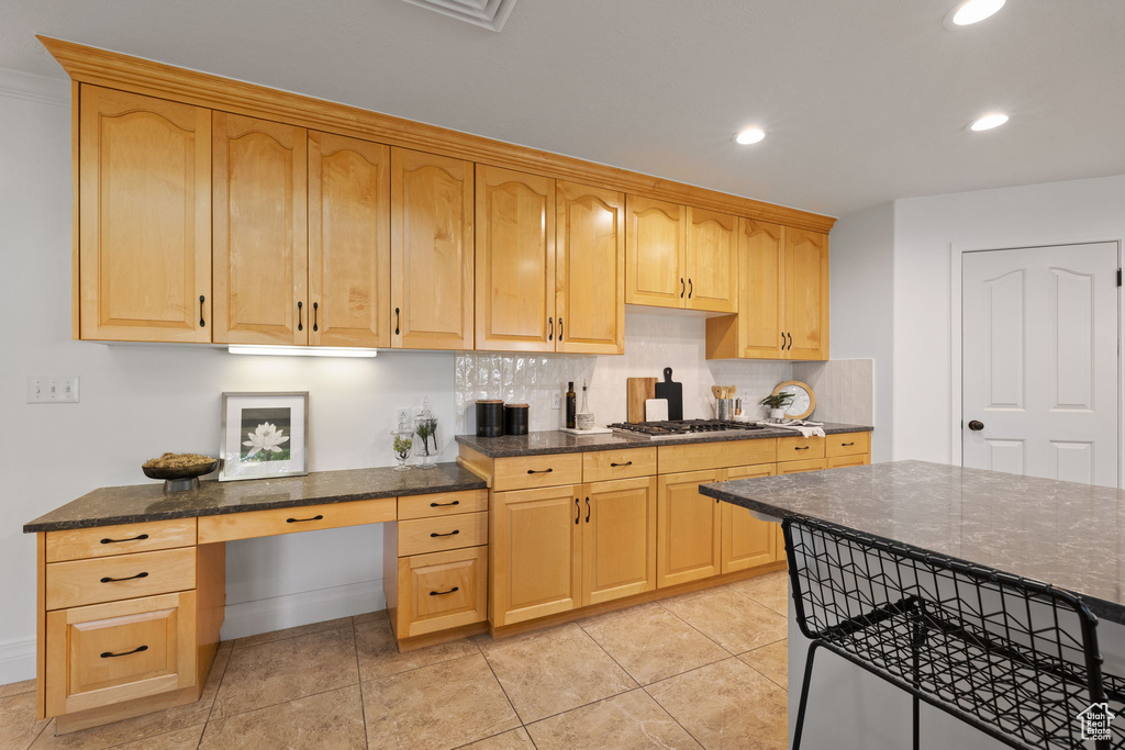 Kitchen with dark stone countertops, tasteful backsplash, stainless steel gas cooktop, recessed lighting, and light brown cabinetry