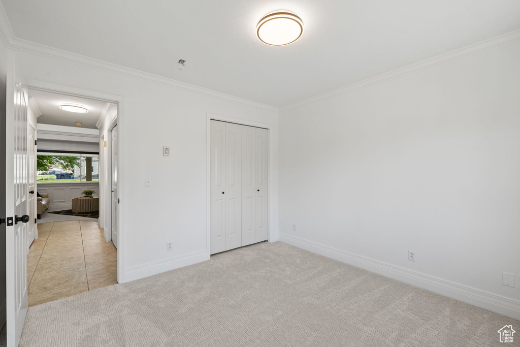 Unfurnished bedroom with crown molding, light carpet, baseboards, and a closet