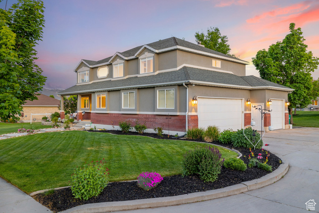View of front of house featuring brick siding, a garage, stucco siding, concrete driveway, and a front lawn
