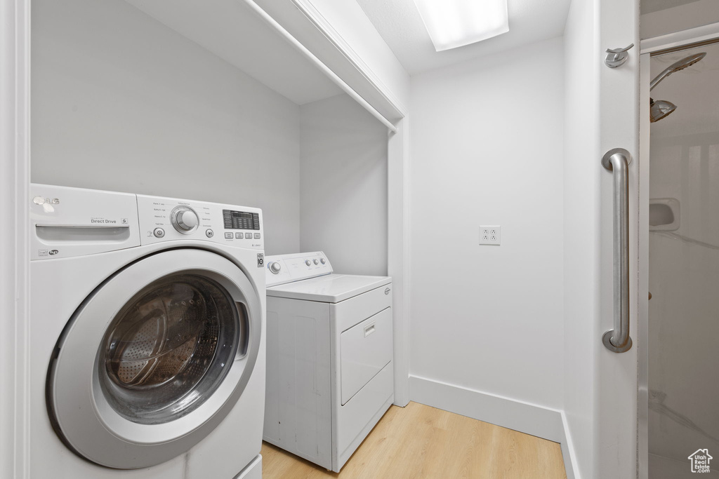 Washroom with light wood-type flooring, washing machine and dryer, and baseboards