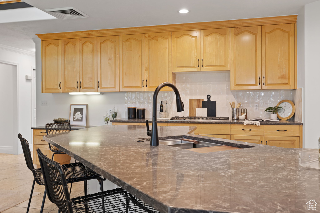 Kitchen featuring light brown cabinetry, decorative backsplash, a sink, ornamental molding, and a kitchen breakfast bar