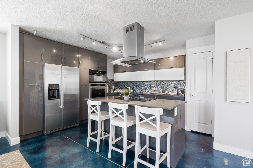 Kitchen featuring stainless steel appliances, baseboards, tasteful backsplash, a breakfast bar, and a textured ceiling