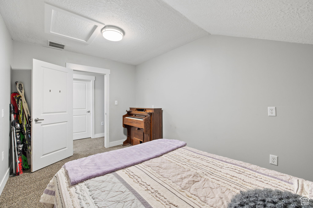Carpeted bedroom with attic access, a textured ceiling, vaulted ceiling, and baseboards