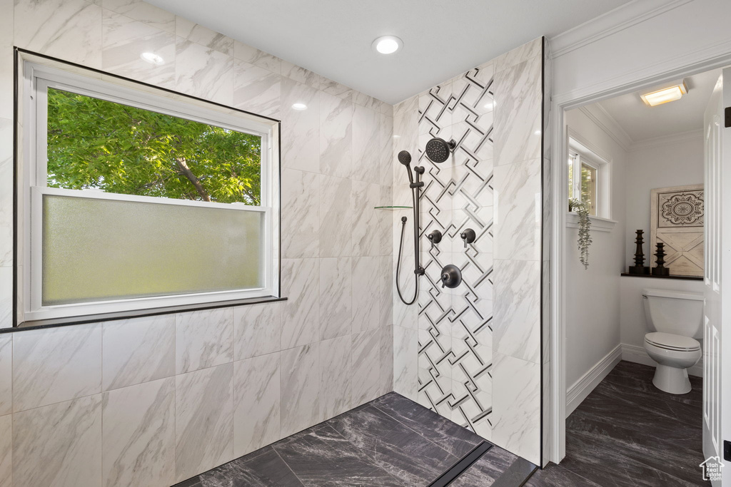 Bathroom with marble tiled floors, ornamental molding, plenty of natural light, tiled shower, and toilet