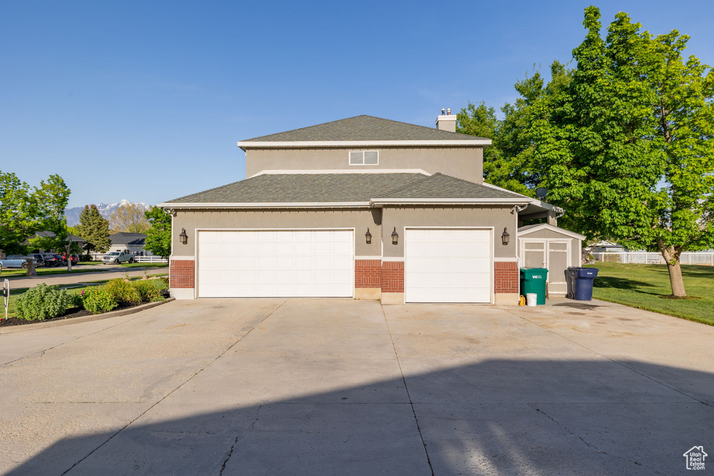 View of front of property featuring driveway, a garage, a storage unit, and stucco siding