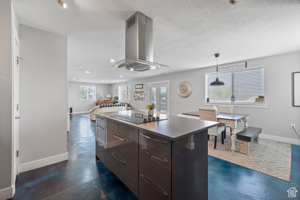 Kitchen featuring island exhaust hood, black electric stovetop, baseboards, modern cabinets, and a textured ceiling