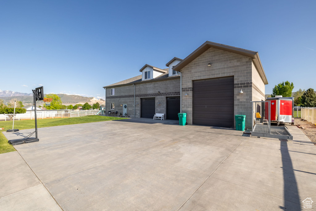 View of property exterior with fence, a mountain view, an attached garage, and concrete driveway