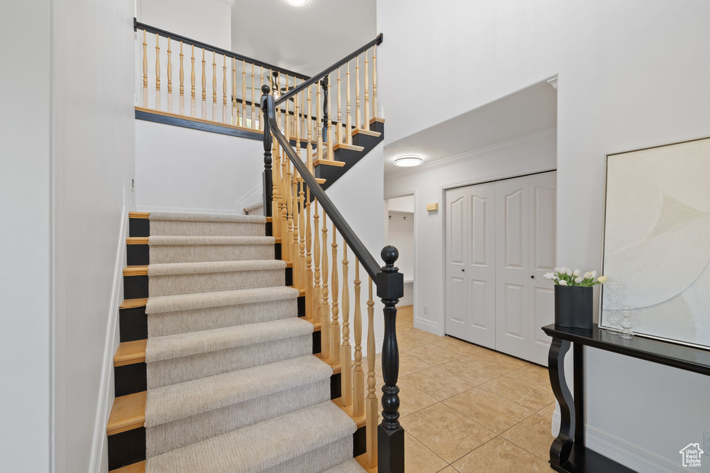 Stairs featuring tile patterned floors, a towering ceiling, crown molding, and baseboards