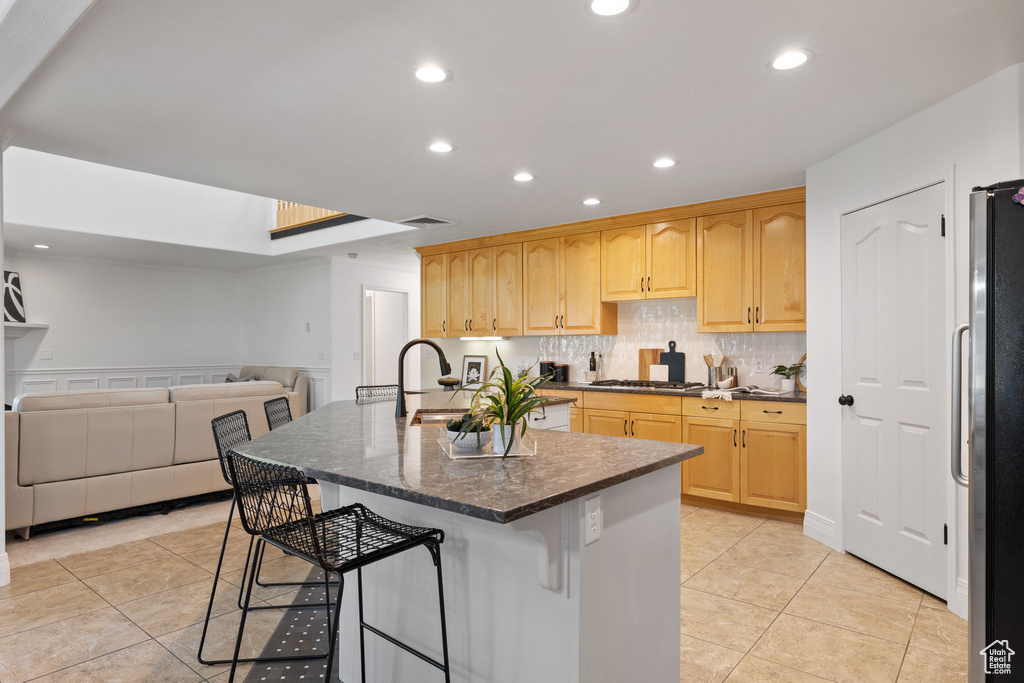Kitchen featuring stainless steel appliances, a sink, a kitchen breakfast bar, open floor plan, and light brown cabinetry