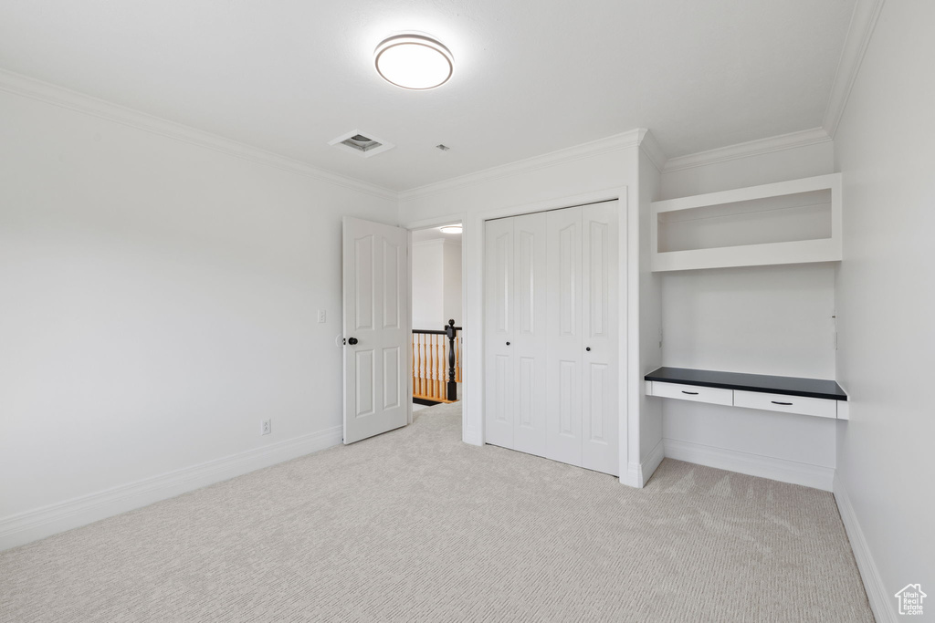 Unfurnished bedroom with crown molding, light carpet, baseboards, a closet, and a desk