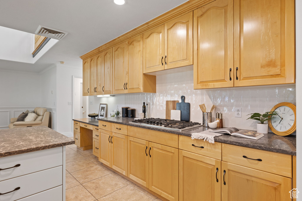 Kitchen with stainless steel gas stovetop, backsplash, dark stone counters, light tile patterned flooring, and ornamental molding