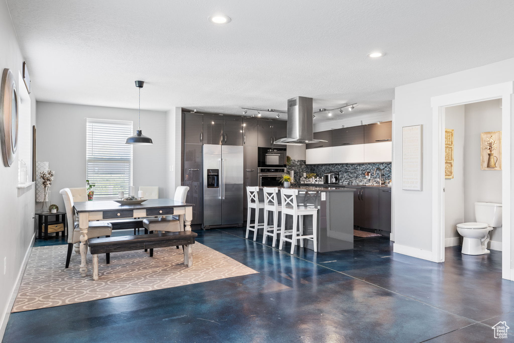 Kitchen with stainless steel refrigerator with ice dispenser, island range hood, finished concrete flooring, decorative backsplash, and recessed lighting
