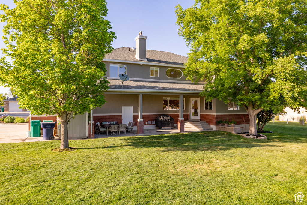 Rear view of property featuring brick siding, a yard, a patio area, and a chimney