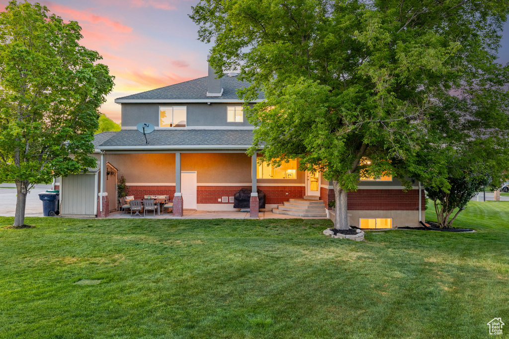 Rear view of property with a patio, brick siding, a yard, a shingled roof, and stucco siding