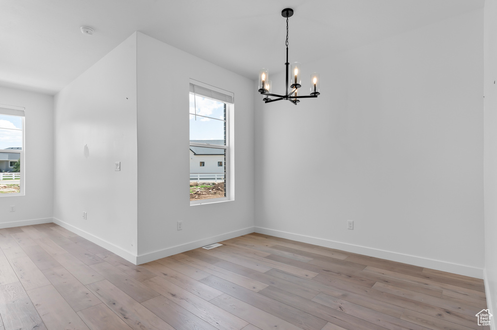 Empty room with a chandelier, light wood finished floors, baseboards, and a smoke detector